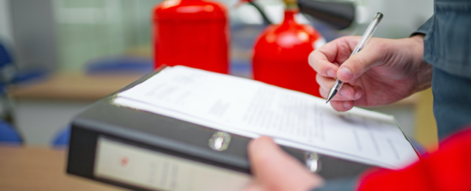 person writing on a notepad in front of fire extinguishers