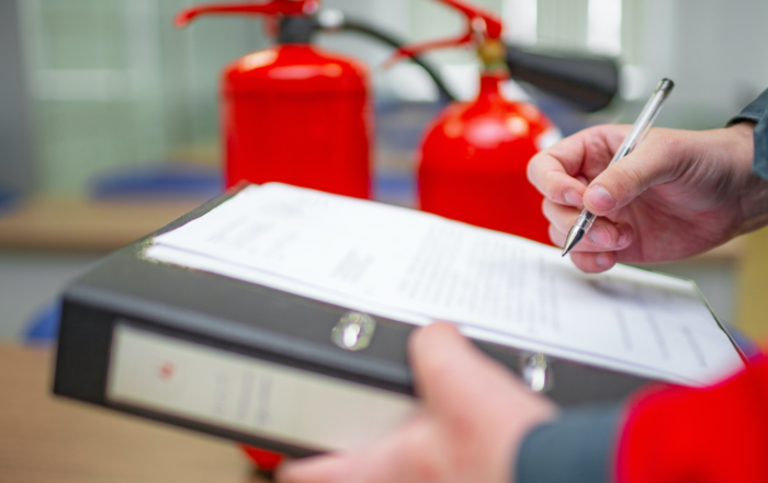 person writing on a notepad in front of fire extinguishers