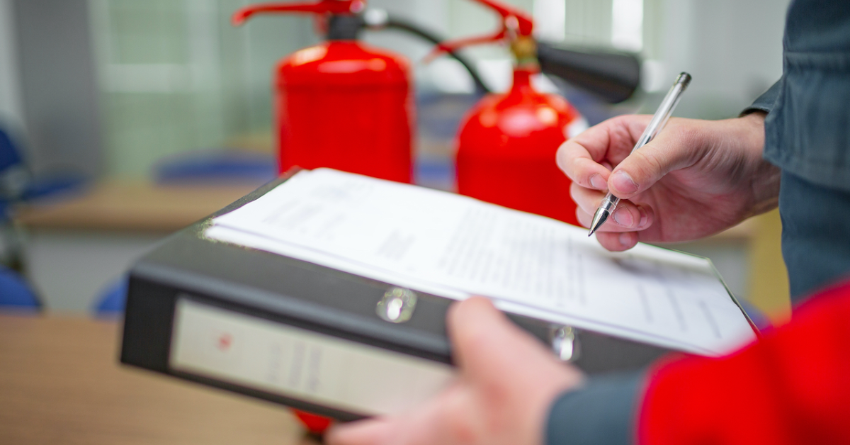 person writing on a notepad in front of fire extinguishers